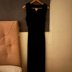 Svart glittrig klänning - Elegant svart klänning med glittrande detaljer. Den har en figurnära passform och är ärmlös, vilket gör den perfekt för festliga tillfällen. Klänningen har en klassisk design som framhäver en stilren look.