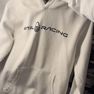 Vit hoodie från Sail Racing - Snygg vit hoodie från Sail Racing med svart logotyp på bröstet. 