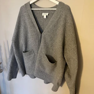 Grå kofta från Monki - Mysig grå kofta från Monki med knappar och två praktiska fickor framtill. Den har en v-ringad design och ribbade kanter som ger en stilren look. Perfekt för kyliga dagar!