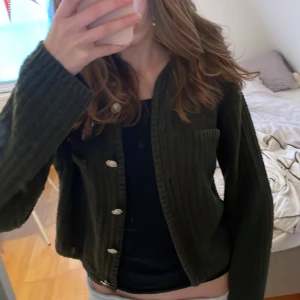 Olivgrön stickad kofta från H&M - Säljer en olivgrön stickad kofta från H&M med snygga silverfärgade knappar. Koftan är ribbad och har långa ärmar,  bra skick och bara perfekt nu i vinter💕kontakta om du har frågor 💕❤️