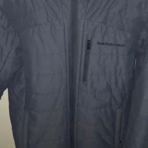 Blå quiltad jacka från Peak Performance stl S  - Snygg blå quiltad jacka från Peak Performance med dragkedja och broderad logga på bröstet. Perfekt för kyligare dagar med sin stilrena design och praktiska fickor.style Oskar J