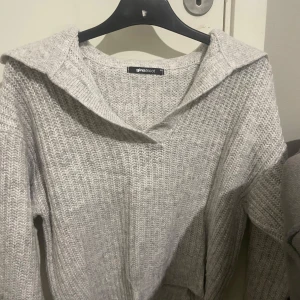 Grå stickad tröja från Gina Tricot - Mysig grå stickad tröja från Gina Tricot med en bred krage och ribbad struktur. Perfekt för kyliga dagar.