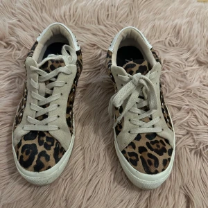 Leopardmönstrade sneakers från Zara - Snygga sneakers från Zara med leopardmönster och beige detaljer. Skorna har snörning och är dekorerade med nitar på hälen. Perfekta för att ge din outfit en trendig touch.