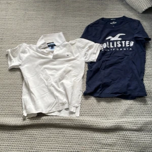 Vit pikétröja från Tommy Hilfiger och marinblå t-shirt från Hollister från Hollister - Säljer en stilren vit pikétröja från Tommy Hilfiger i storlek M och en marinblå t-shirt med tryck från Hollister i storlek XS. Pikétröjan har klassisk krage och korta ärmar, medan t-shirten har en 'muscle fit' passform. Tommy Hilfiger 200kr och Hollister 150kr