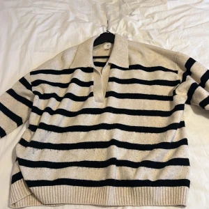 Randig tröja från H&M - Säljer en snygg randig tröja från H&M i beige och svart. Tröjan har en klassisk krage och ribbade muddar vid ärmslut och nederkant. Perfekt för en avslappnad stil.