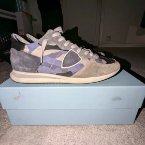 Camouflage sneakers från Philippe Model - Snygga sneakers från Philippe Model med ett unikt camouflage-mönster i blått, grått och beige. Skorna har snörning och en stilren design som passar perfekt för en trendig look.