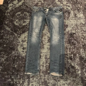 Blå jeans från Replay - Snygga blå jeans från Replay, modell Grover. De har en klassisk femficksdesign med knappgylf och slitna detaljer för en cool look. Perfekta för en avslappnad stil.