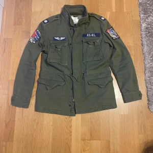 grön ralph lauren fieldjacket - En riktigt snygg helt ny militärgrön ralph lauren field jacket med prislappen kvar. Nypris är 5000kr mitt pris 3000kr! Den är i storlek S men är stor i storleken så passar även M. Är själv 185cm ca 75 kg och passar perfekt. Pris kan diskuteras!