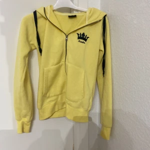 Gul hoodie från On The Peak - Säljer en superfin gul hoodie från On The Peak i storlek XS. Den har en dragkedja framtill och en snygg broderad krona med texten 'Sweden' på bröstet. Huvan har också 'Sweden' broderat på baksidan. Perfekt för att visa lite svensk stolthet! 💛