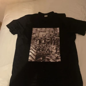 Svart t-shirt från C.P. Company - Säljer en svart t-shirt från C.P. Company med ett coolt tryck på framsidan. T-shirten är del av 'The Metropolis Series' och har en normal passform. Perfekt för vardagsbruk eller en avslappnad utekväll. Är storlek XXL men är som en XL
