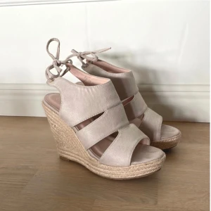 Beige kilklackssandaler med snörning - Snygga och sköna kilklackar i beige mocka med snörning runt vristen. Perfekt skick! (Använda en gång) Storlek 39