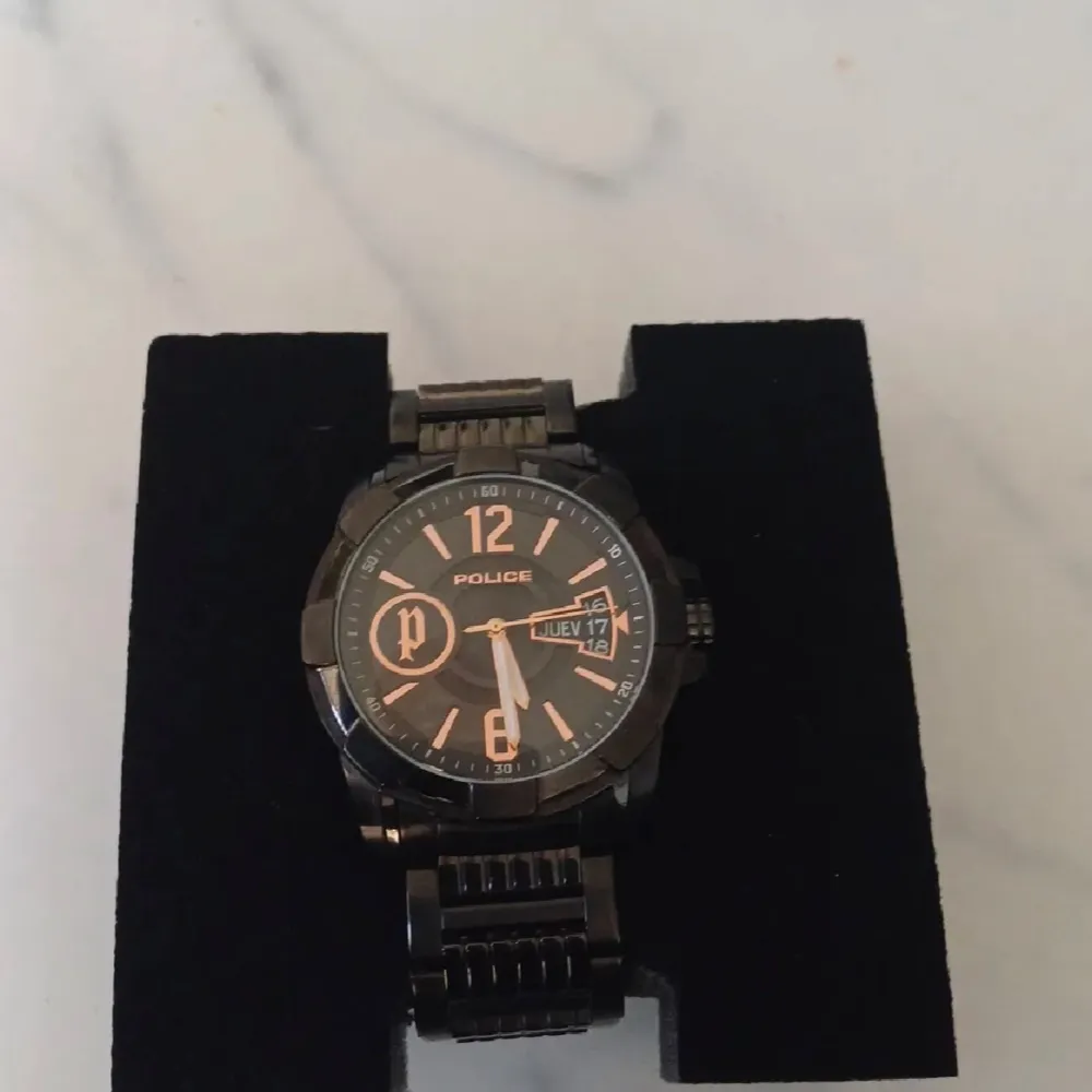 Säljer en snygg svart klocka från Police. Den har en robust design med en svart urtavla och tydliga siffror. Klockan visar både datum och veckodag, vilket är superpraktiskt. Armbandet är också svart och i metall, vilket ger en cool och stilren look. Perfekt för både vardag och fest!. Asusteet.