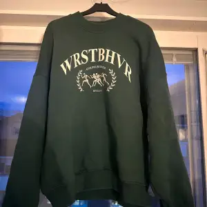 Säljer en snygg grön sweatshirt från WRSTBHVR i storlek M. Tröjan har ett vintage liknande tryck på framsidan med texten 'WRSTBHVR' och en häftig design. Den är tyvärr för liten för mig, och endast använd ett fåtal gånger.