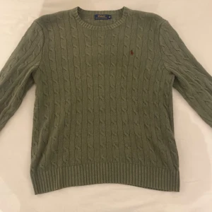 Grön stickad tröja från Polo Ralph Lauren - Säljer en snygg grön stickad tröja från Polo Ralph Lauren. Den är i storlek M och har ett klassiskt kabelstickat mönster. Tröjan är tillverkad i 100% silke vilket gör den supermjuk och lyxig. Perfekt för höst och vinter!