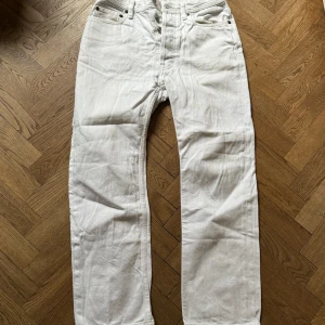 Vita jeans från Acne Studios - Säljer ett par snygga vita jeans från Acne Studios, Blå Konst-kollektionen. De är i storlek 26 och har en klassisk design med knappar i gylfen. Perfekta för en stilren look!