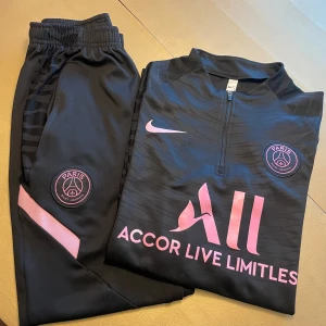 psg tracksuit - Snygg svart fotbollströja från Nike med Paris Saint-Germain-logga i rosa. Tröjan har en halv zip och rosa detaljer, inklusive texten 'Accor Live Limitless'. Perfekt för fans av PSG!