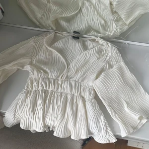 Vit blus från Gina Tricot - Säljer en elegant vit blus från Gina Tricot i storlek XS. Blusen har en v-ringad design med långa ärmar och ett fint plisserat mönster. Perfekt för en stilren look.💓
