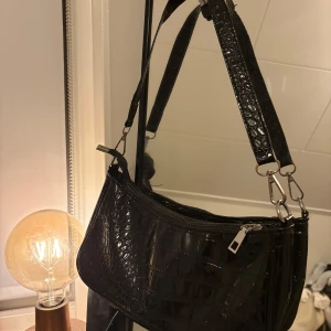 Svart axelväska med krokodilmönster - Snygg svart axelväska med krokodilmönster, dragkedja och ett fack inuti.