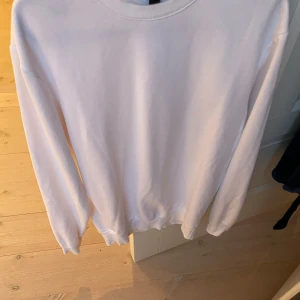 Vit långärmad tröja - Säljer en stilren vit långärmad tröja. Perfekt för en enkel och avslappnad look. Tröjan har en rund halsringning och ribbade muddar vid ärmslut och nederkant.