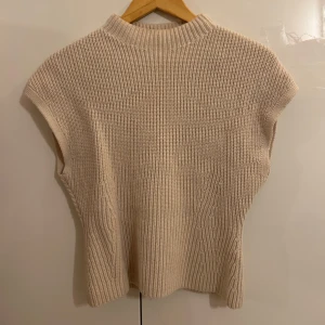 Beige stickad ärmlös tröja från &otherstories - Säljer en stilren beige stickad tröja från &otherstories . Den är ärmlös med en hög krage och har en mjuk och bekväm passform. Lappen är av klippt.