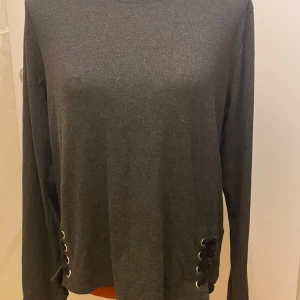 Mörkgrå tröja från FB Sister XL - Snygg mörkgrå tröja från FB Sister i storlek XL. Tröjan har långa ärmar och coola snörningsdetaljer på sidorna. Perfekt för en stilren look. Längd: 61 cm Armhåla till armhåla: 54 cm  Inga bilder när den sitter på mig! Katter finns i hemmet