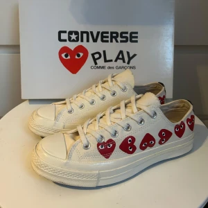 Converse Play Comme des Garçons sneakers - Snygga vita Converse Play sneakers i samarbete med Comme des Garçons. Skorna har det ikoniska röda hjärtmotivet längs sidorna och klassisk snörning. Perfekta för en stilren look. Skorna är i väldigt bra skick använda ett fåtal gånger, köptes på NK i somras för 2100 kr. Säljer pga att de inte kommer till användning. (Endast skor ingår) 
