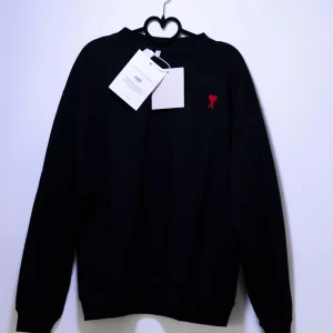 Ami Paris Sweatshirt - Nästan helt ny Ami Paris Sweatshirt med ett märke på bröstet. Tröjan har långa ärmar och en klassisk passform. Perfekt för en stilren look. Finns fler storlekar i min profil😁