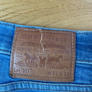 Levi's 511 jeans i blå denim - Snygga Levi's 511 jeans i klassisk blå denim. De har en normal passform med en rak silhuett och är tillverkade i slitstarkt jeanstyg. Perfekta för en avslappnad stil med fem fickor och knappgylf. Kan diskutera pris vid snabb affär! De är bara att fråga om mer information.