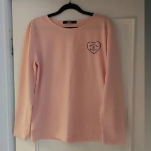 Rosa långärmad tröja från Bik Bok - Säljer en söt rosa långärmad tröja från Bik Bok med ett hjärtmotiv och texten 'You & Me Forever' på bröstet. Perfekt för en avslappnad stil.