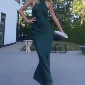 Mörkgrön axelbandslös långklänning - Elegant mörkgrön långklänning med en stilren design. Klänningen är axelbandslös och har en snygg snörning. Perfekt för speciella tillfällen. Helt oanvänd