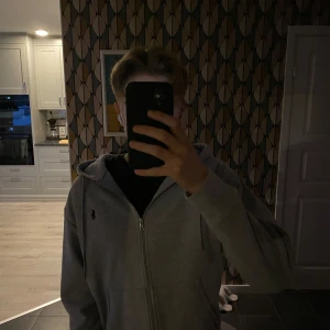 Grå hoodie från Polo Ralph Lauren - Säljer en stilren grå hoodie från Polo Ralph Lauren med dragkedja och broderad logga på bröstet. . Den har en klassisk passform och är tillverkad i mjukt material. Säljer då den aldrig riktigt passat mig,