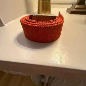 Orange bälte från Helly Hansen - Snyggt orange bälte från Helly Hansen med en robust metallspänne. Perfekt för att ge en färgklick till din outfit. Bältet har en enkel och stilren design som passar till många olika stilar. 120 cm. Mycket bra skick.