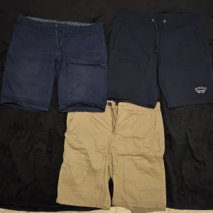 Tre par shorts i olika färger - Säljer tre par shorts: ett par mörkblå shorts med dragkedja, ett par marinblå mjukisshorts med snörning och ett par beige shorts med dragkedja. Perfekta för sommaren!