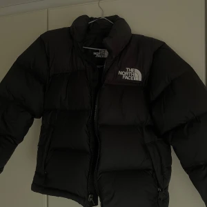 Svart dunjacka från The North Face - (PRIS GÅR ATT DISKUTERA!)Säljer en svart pufferjacka från The North Face. Jackan har en hög krage och dragkedja framtill. Perfekt för kalla dagar med sin vadderade design.