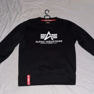 Svart sweatshirt från Alpha Industries - Snygg svart sweatshirt från Alpha Industries med deras ikoniska logga tryckt på framsidan. 