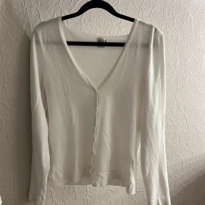 Vit kofta från Saint Tropez - Säljer en stilren vit kofta från Saint Tropez med v-ringning och knappar framtill. Perfekt för lager-på-lager och passar till många olika outfits.