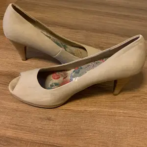 Säljer ett par e beige pumps i  bra skick. De har en öppen tå och en bekväm klack. Insidan är klädd med ett färgglatt blommigt mönster som ger en fin kontrast. Perfekta för både vardag och fest!