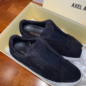Svarta sneakers från Axel Arigato - Säljer ett par stilrena svarta sneakers från Axel Arigato. De är i bra skick med en snygg och enkel design. Skorna är gjorda i mocka och har en vit sula som ger en fräsch kontrast. Perfekta för både vardag och fest!    OBS‼️ har ej boxen kvar till dom