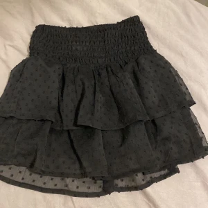 Svart volangkjol från H&M - Säljer en superfin svart volangkjol från H&M i storlek 140. Kjolen har ett sött prickigt mönster och elastisk midja för en bekväm passform. Perfekt för både vardag och fest! 🖤