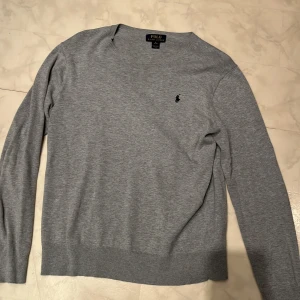 Grå tröja från Polo Ralph Lauren - Säljer en stilren grå tröja från Polo Ralph Lauren i mycket bra skick. Den har en klassisk design med långärmade ärmar och en liten broderad logga på bröstet. Perfekt för både vardag och lite finare tillfällen. Passar bra till höst och vår!