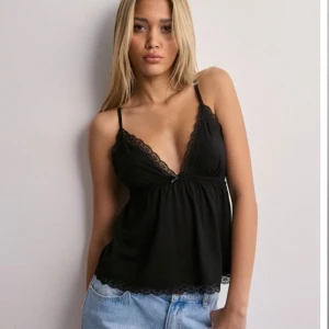 Svart topp med spetsdetaljer - Svart topp med smala axelband och v-ringning. Toppen har fina spetsdetaljer längs kanterna och en lös passform som ger en avslappnad look. Från Nelly. Nypris 249
