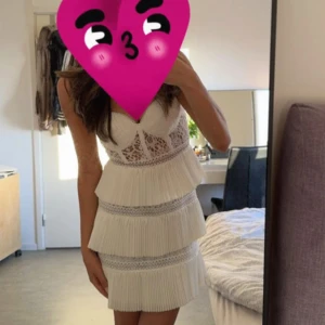 Vit spetsklänning med volanger - Säljer en superfin vit klänning med spetsdetaljer och volanger. Den är ärmlös och perfekt för sommarens fester. Klänningen har en tight passform och är i mycket bra skick. Perfekt för studenten💕den har dock missfärgat pågrund av champagne 
