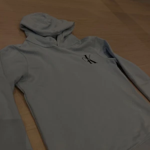 Ljusblå hoodie från Calvin Klein 200kr - Säljer en stilren Ljusblå hoodie från Calvin Klein i storlek som passar en 13-14 åring. Den har en klassisk design med en CK-logga på bröstet. Perfekt för både vardag och chill. Den är i mycket bra skick och bekväm att ha på sig. Passar perfekt till jeans eller mjukisbyxor! Pris går att diskutera.