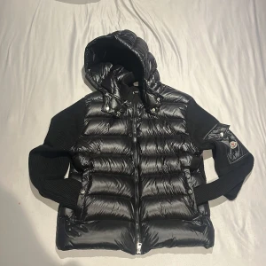 Moncler cardigan - Säljer en snygg svart pufferjacka med huva. Jackan har en glansig finish och är perfekt för kyliga dagar. Den har dragkedja framtill och ribbade ärmar för extra komfort. Perfekt för höst och vinter!. Storlek xl men liten i stolek så passar mer L/M