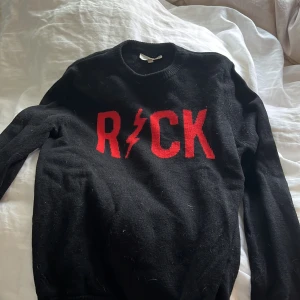 Svart tröja med röd text från Zadig & Voltaire - Säljer en cool svart tröja från Zadig & Voltaire med röd text 'ROCK' och en blixt på framsidan. Tröjan är i mycket bra skick och perfekt för höst och vinter. Den har långa ärmar och är supermjuk och bekväm. Perfekt för att ge din outfit en rockig touch! 🤘
