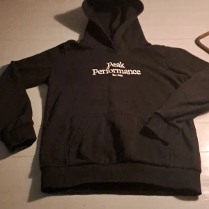 Svart hoodie från Peak Performance - Säljer en svart hoodie från Peak Performance i mycket bra skick. Den har en klassisk design med vit logga på bröstet och en mysig huva. Perfekt för både vardag och träning. Passar bra till höst och vinter! Andvänd max 8 gånger. Nypris 700.