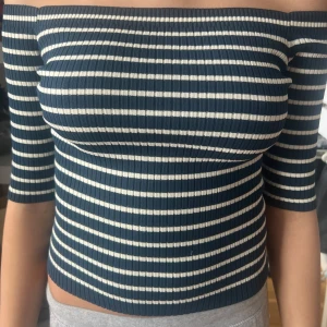 Randig offshoulder topp - Snygg randig offshoulder topp i blått och vitt. Den är ribbad och har trekvartsärmar, perfekt för en somrig look. Passar både till vardags och fest!