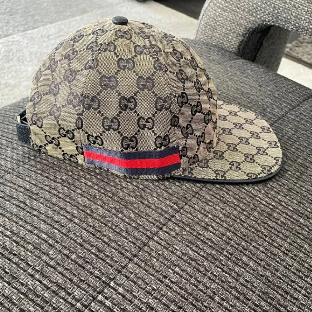 Säljer en snygg keps från Gucci med deras ikoniska mönster i beige och svart. Kepsen har en justerbar rem baktill och en röd och grön randdetalj. Perfekt för att ge din outfit en lyxig touch. Kommer i originalförpackning.. Accessoarer.