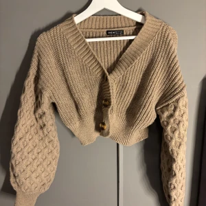 Beige stickad kofta från SHEIN - Säljer en superfin beige stickad kofta från SHEIN. Den har en v-ringad design med stora knappar framtill och ett snyggt mönster på ärmarna. Perfekt för höst och vår när du vill vara både varm och stilren. Passar perfekt till jeans eller kjol!