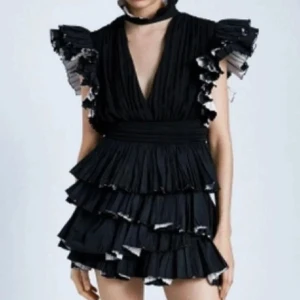 Svart volangklänning med djup V-ringning - Säljer en superfin svart klänning med volanger och djup V-ringning. Den har korta ärmar med volangdetaljer och en flerdelad kjol som ger en härlig volym. Perfekt för festliga tillfällen! 🖤